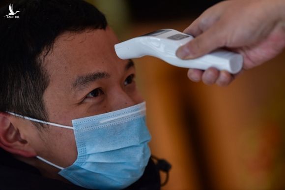 Nhân viên y tế kiểm tra thân nhiệt một người đàn ông tại một tòa nhà ở Vũ Hán ngày 26.1 /// AFP