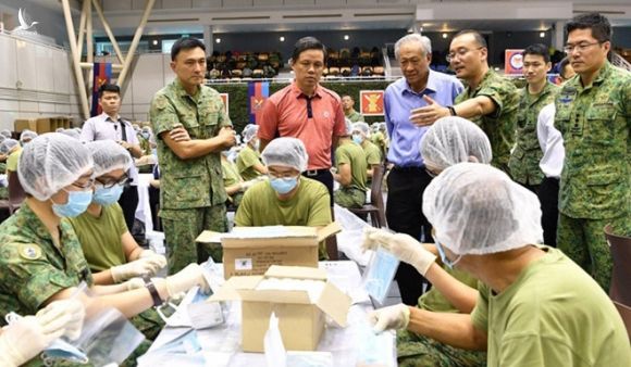 Bộ trưởng Singapore Chan Chun Sing (áo cam) xem các quân nhân chuẩn bị khẩu trang để phân phát /// Reuters.