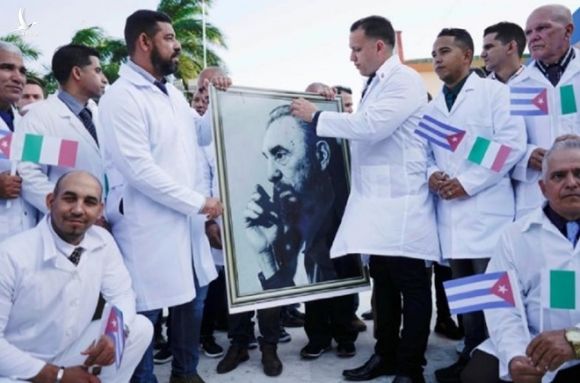 Các bác sĩ Cuba giữ di ảnh cố lãnh tụ Fidel Castro trong buổi lễ chia tay trước khi lên đường đến Ý để hỗ trợ chống lại đại dịch COVID-19 tại thủ đô Havana ngày 21.3 /// Reuters