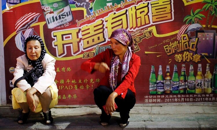 Hai phụ nữ dân tộc Duy Ngô Nhĩ ngồi trước một biển quảng cáo bia gần chợ ở Kashgar, Tân Cương tháng 8/2011. Ảnh: Reuters.
