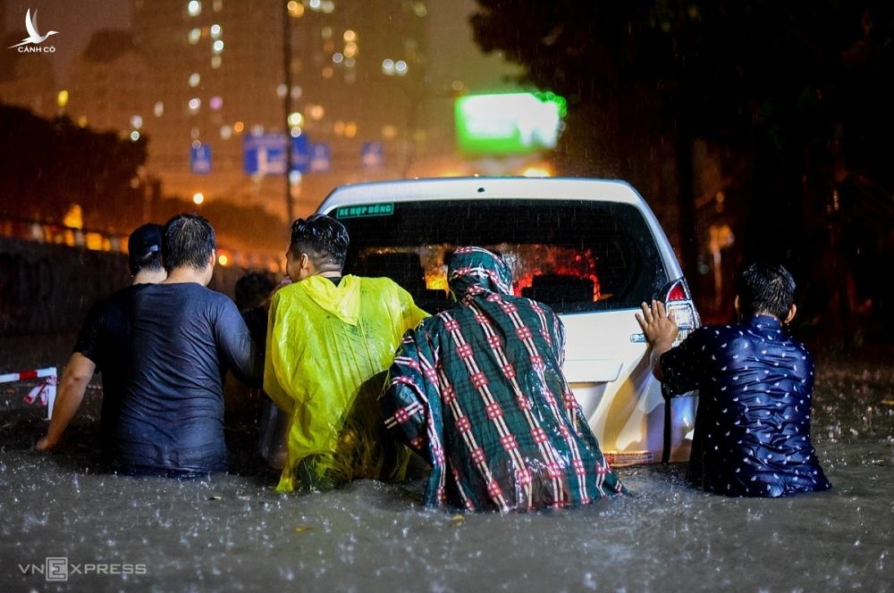 Người đi đường và dân trong khu vực dầm mưa, hợp sức giúp tài xế đẩy ôtô qua đoạn ngập sâu.