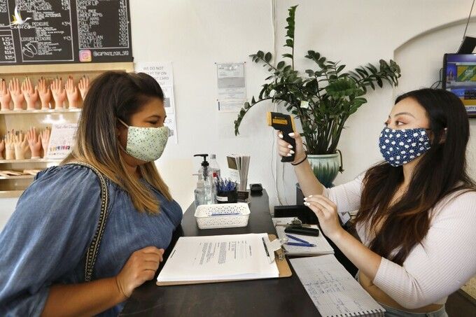 Nhân viên đo thân nhiệt cho khách tại tiệm Captivate Nail & Spa ở thành phố Fullerton, bang California, hôm 19/6. Ảnh: LA Times.