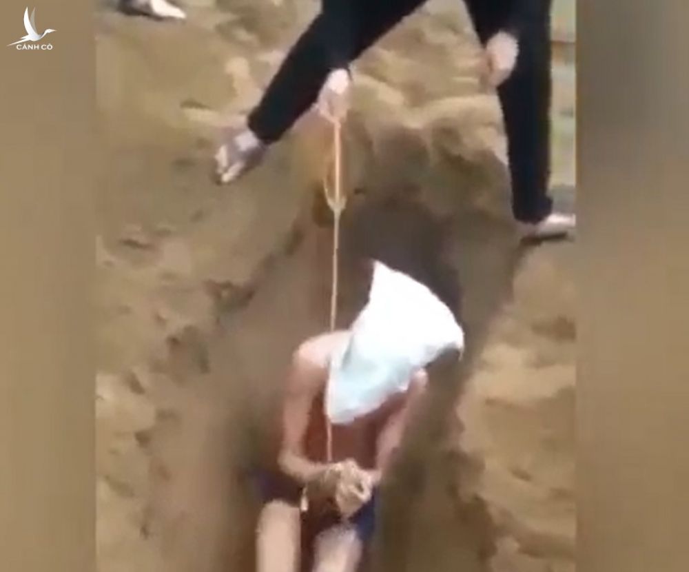 Hình ảnh một thanh niên bị nhóm người bịt mặt, trói tay, ngồi dưới hố cát. Ảnh cắt từ clip.