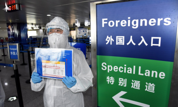 Nhân viên mặc đồ bảo hộ nhắc nhở công dân nước ngoài làm thủ tục ở sân bay Trung Quốc hôm 10/3. Ảnh: Xinhua.
