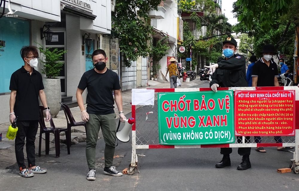 Lực lượng tình nguyện viên và công an chốt bảo vệ vùng xanh hướng dẫn người dân nhận hàng hóa tại cổng chính cư xá Đô Thành. Ảnh: Hà An.