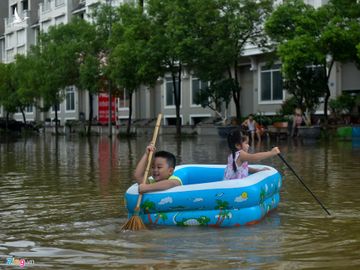 Chiều 4/8, hai trẻ nhỏ Đan Dũng (8 tuổi) và Bảo An (4 tuổi) được bố mẹ mang thuyền phao bơi ngay trước cửa nhà. Chổi tre và gậy đánh gôn là mái chèo của 2 bé. 