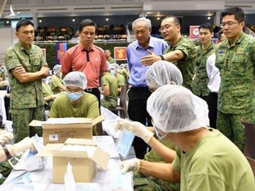 Bộ trưởng Singapore Chan Chun Sing (áo cam) xem các quân nhân chuẩn bị khẩu trang để phân phát /// Reuters.