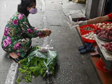 Người phụ nữ mu hàng và chủ quán đều đeo khẩu trang, thực hiện giãn cách xã hội. Ảnh: AFP.