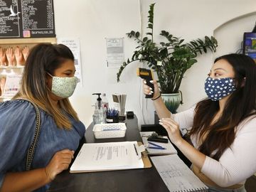 Nhân viên đo thân nhiệt cho khách tại tiệm Captivate Nail & Spa ở thành phố Fullerton, bang California, hôm 19/6. Ảnh: LA Times.