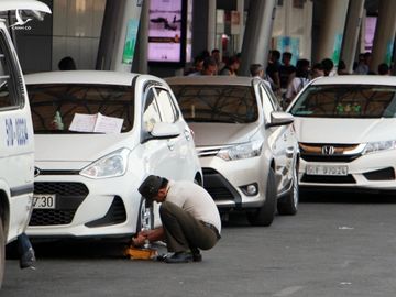 Nhân viên an ninh sân bay Tân Sơn Nhất khoá bánh một ôtô, chờ cẩu đi do đậu quá thời gian trên làn A nhưng tài xế không có mặt, năm 2018. Ảnh:Gia Minh.