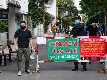 Lực lượng tình nguyện viên và công an chốt bảo vệ vùng xanh hướng dẫn người dân nhận hàng hóa tại cổng chính cư xá Đô Thành. Ảnh: Hà An.