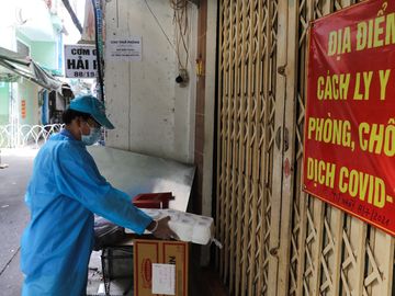 Tình nguyện viên tiếp tế nhu yếu phẩm cho từng nhà có người cách ly y tế trong khu phong toả trên đường Vườn Chuối, quận 3, TP HCM, ngày 30/7. Ảnh: Quỳnh Trần